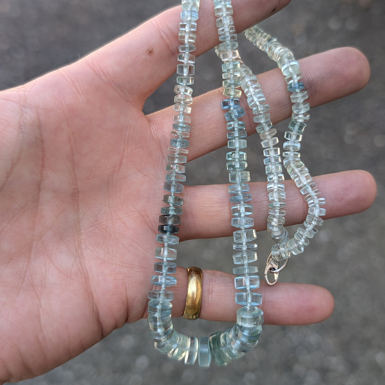 Hand holding beaded aquamarine necklace on a concrete surface