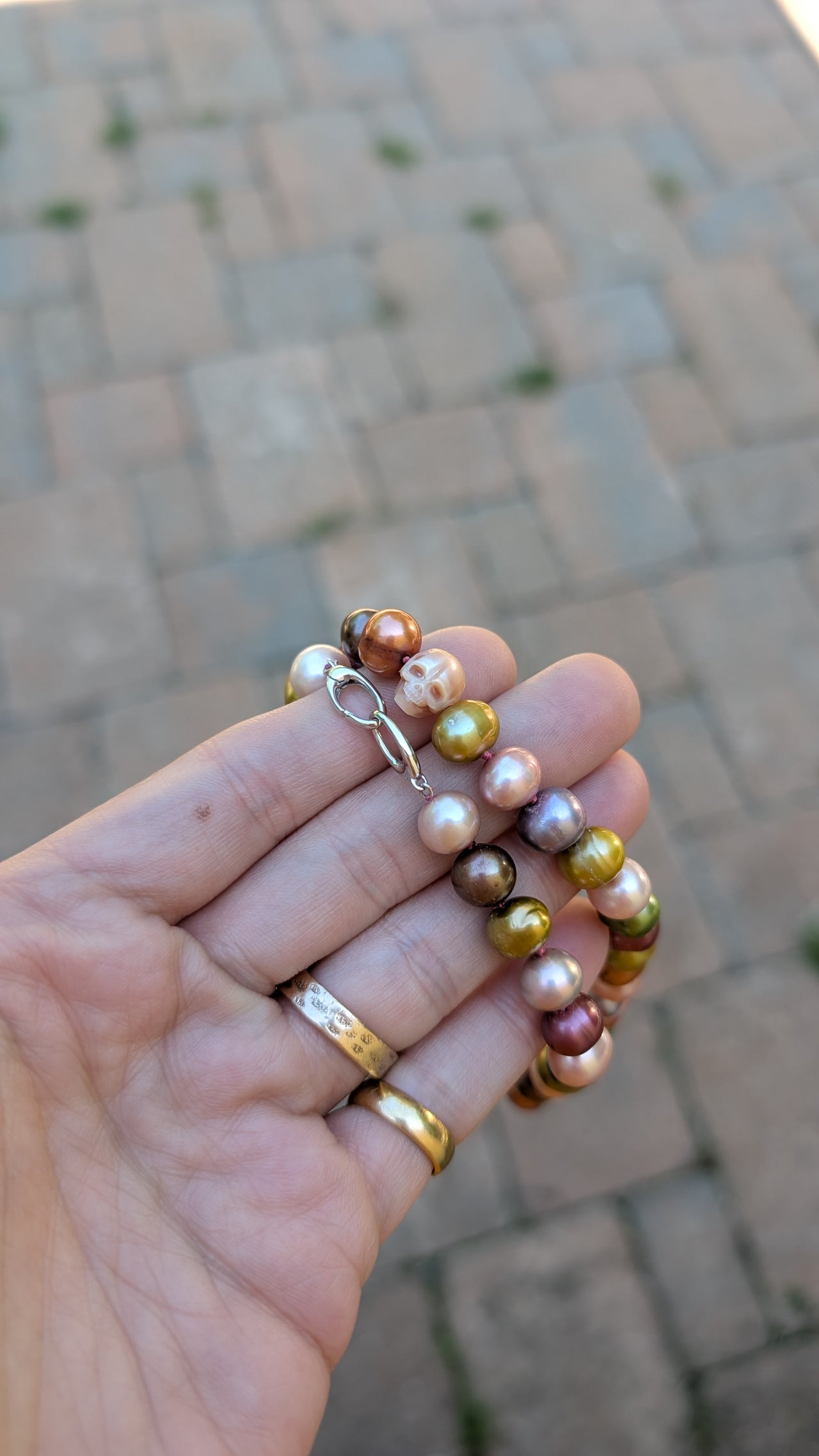 Hand holding a pearl necklace with a blurred pavement background