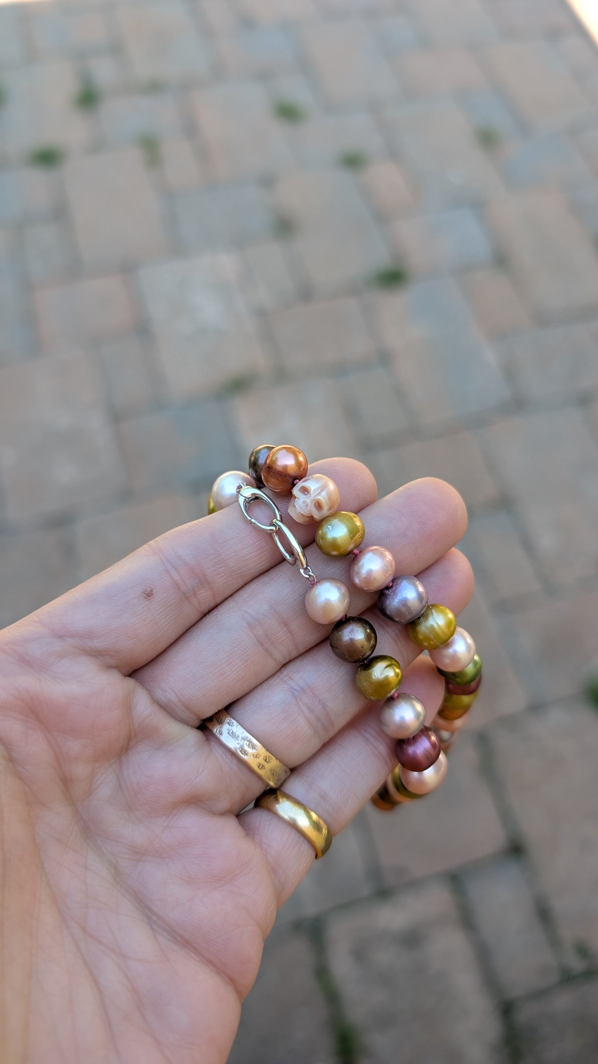Hand holding a pearl necklace with a blurred pavement background