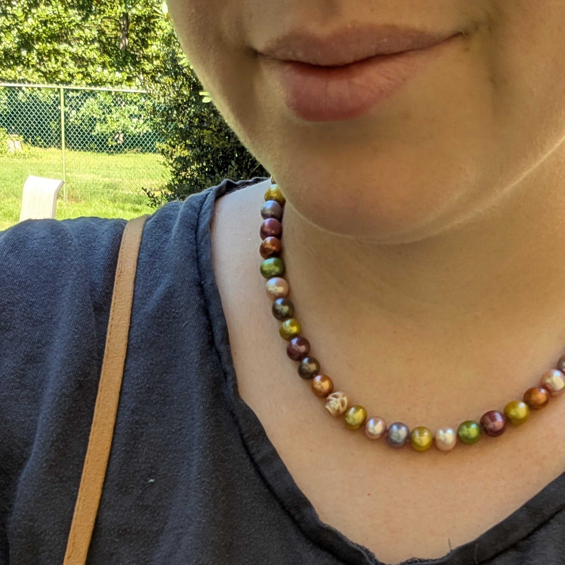 Person wearing a blue shirt with 'I LOVE' text and a beaded necklace, outdoors.