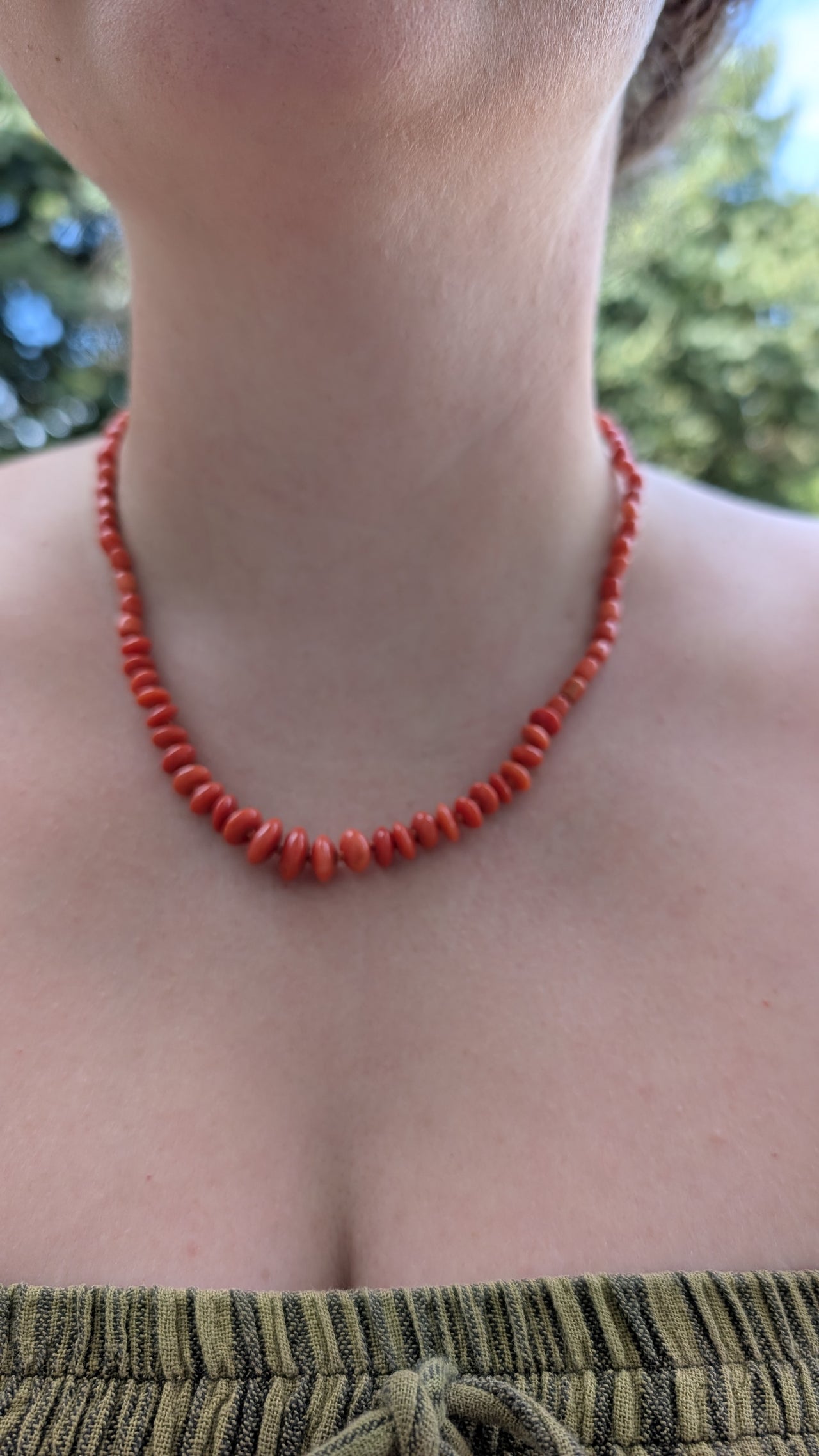 Person wearing a red coral beaded necklace with a blurred natural background