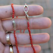 Red beaded necklace with a silver clasp held between fingers against a blurred background