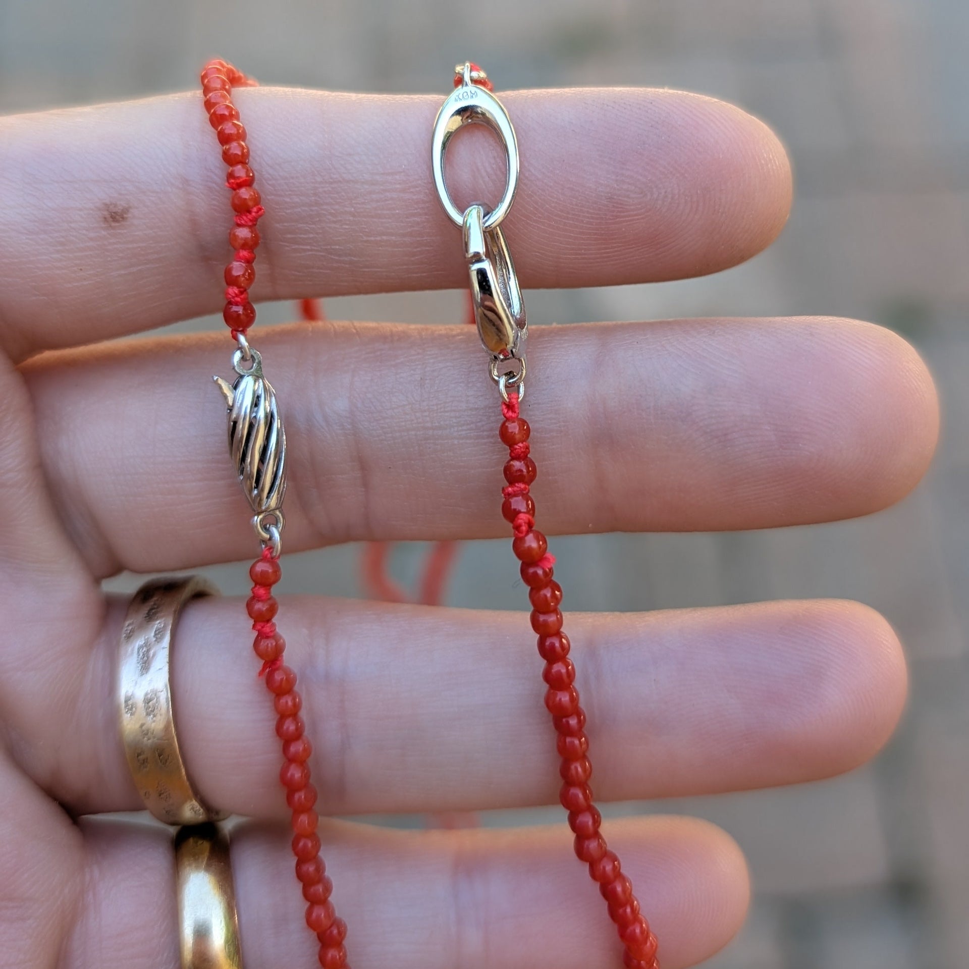 Red beaded necklace with a silver clasp held between fingers against a blurred background
