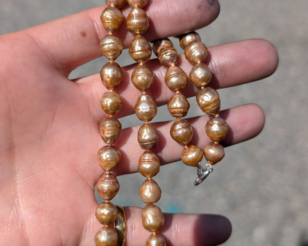Hand holding a string of pearls against a neutral background