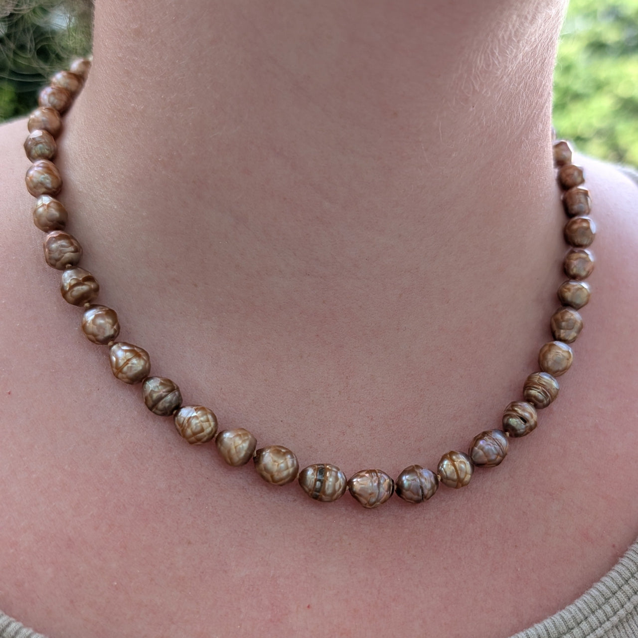 Person wearing a beaded necklace with a blurred natural background
