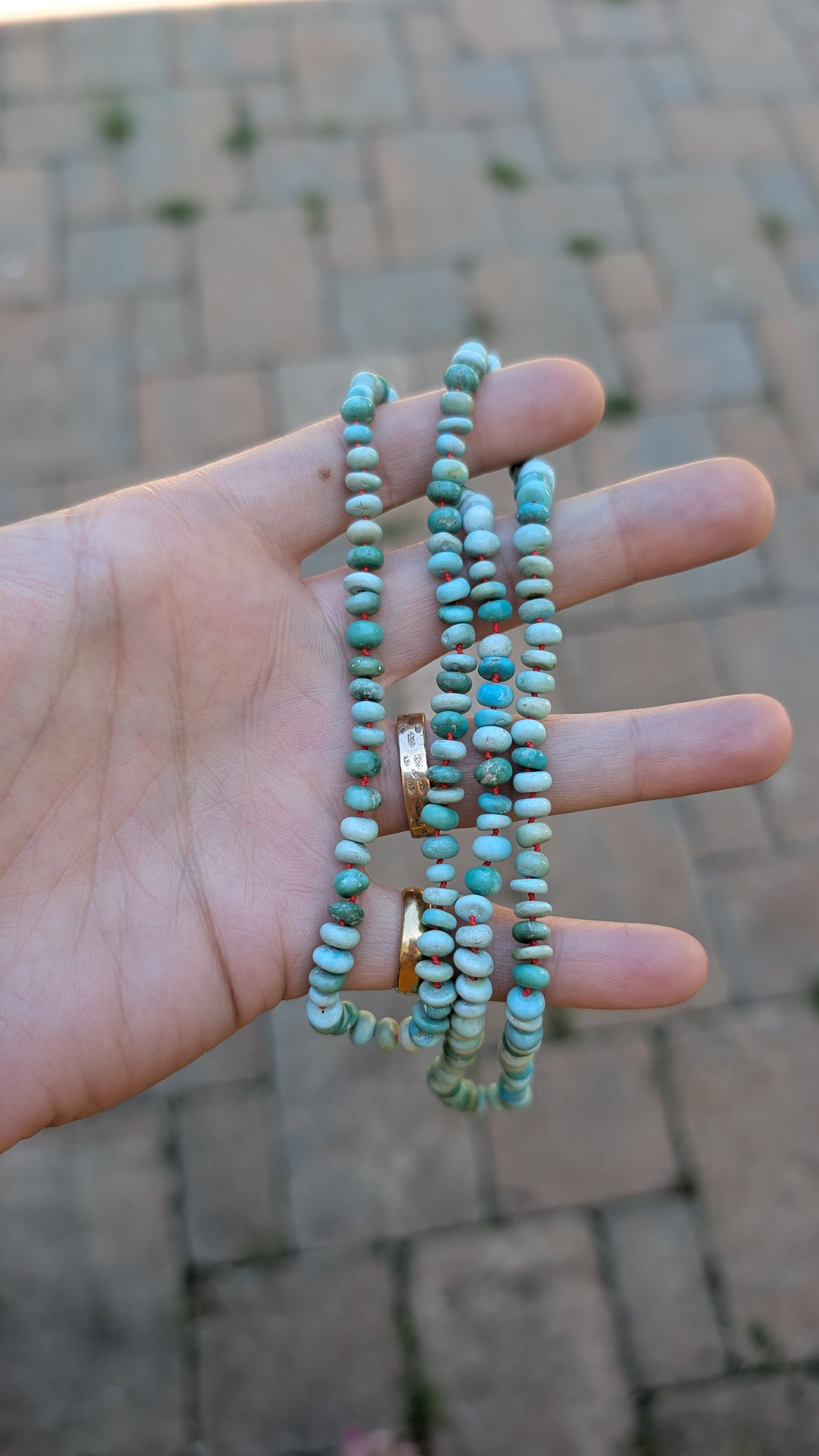 Hand holding three turquoise beaded necklaces against a blurred brick wall background