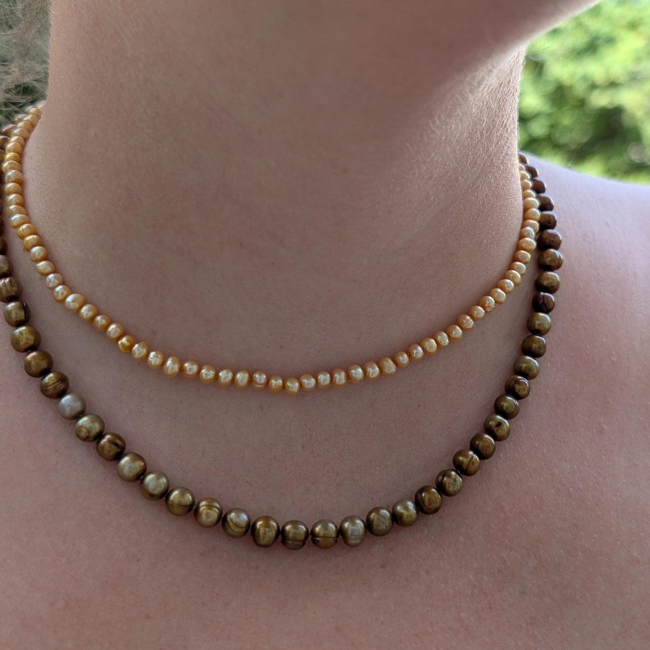 Close-up of a person wearing two beaded necklaces with a blurred natural background