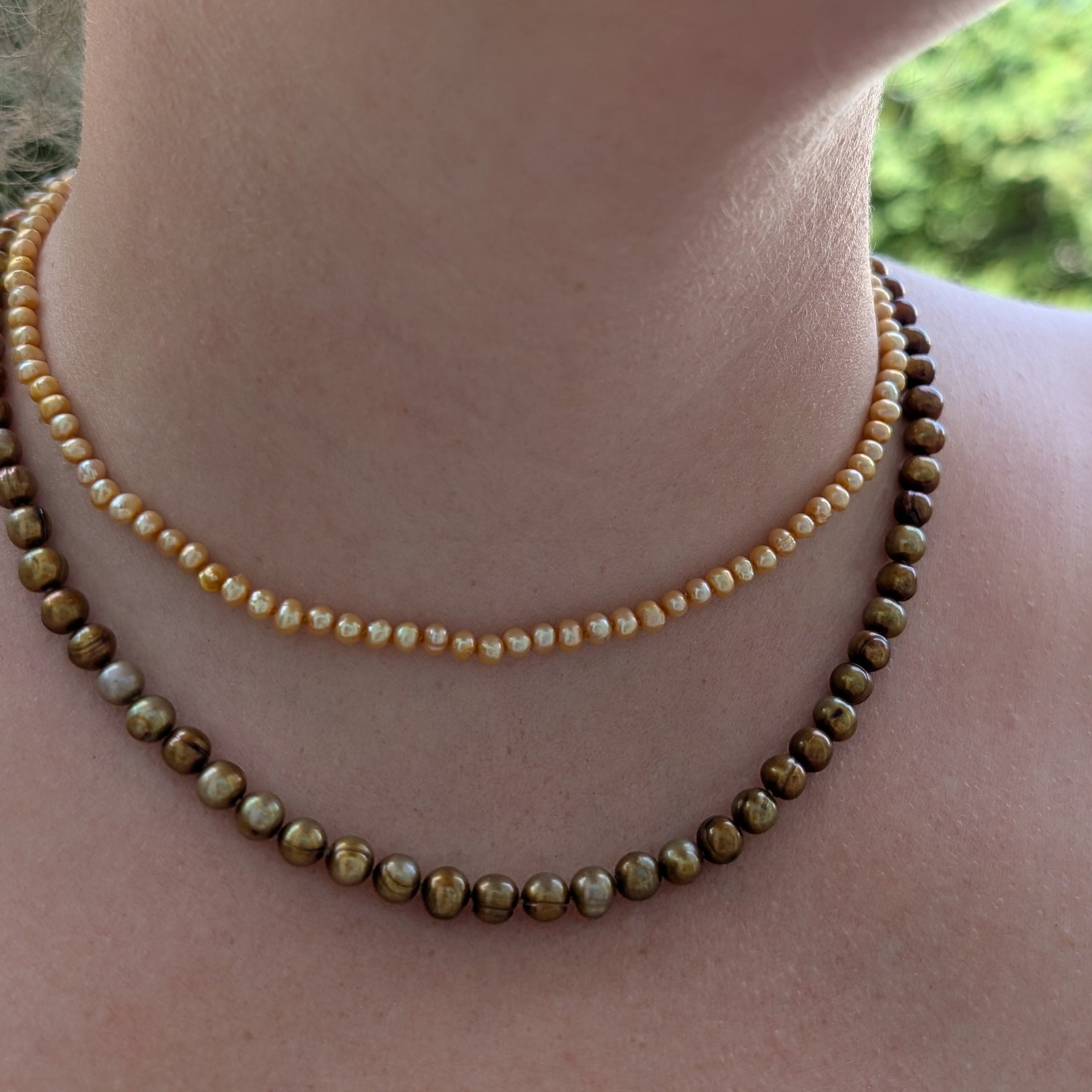 Close-up of a person wearing two beaded necklaces with a blurred natural background